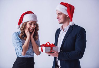 Yakışıklı ve güzel kız ofis giyim ve Santa şapka hediye kutusu tutuyorsun ve gülümseyen, üzerinde beyaz izole.