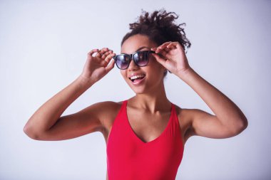 Parlak pembe mayolu ve güneş gözlüklü güzel kız kameraya bakıyor ve gülümsüyor, beyaz tenli.