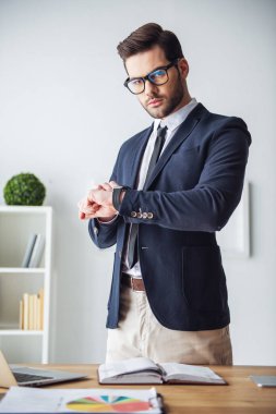 Gözlük yakışıklı işadamı saatini dururken ofiste onun işyerinde bakıyor