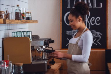 Önlük güzel Afro Amerikan barista kahve kahve makinesi kullanarak yaparken gülümsüyor