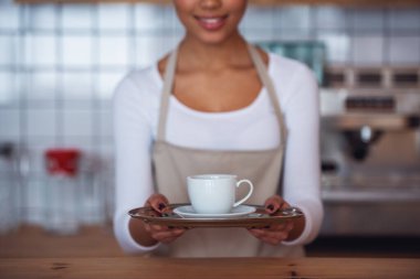 Bir fincan tutarak ve sayaç bar, dururken gülümseyen önlük güzel Afro Amerikan barista kırpılmış görüntü