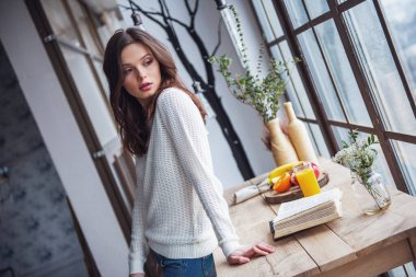 Güzel genç kız rahat kıyafetler içinde uzak evde ahşap masanın üzerine eğilerek arıyor