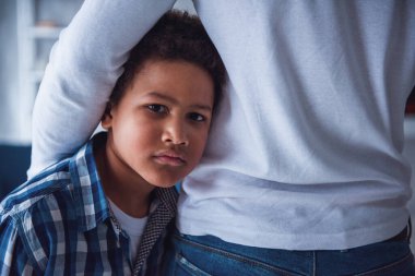 Sıradan giyinmiş üzgün çocuk babasına sarılırken kameraya ciddi ciddi bakıyor.