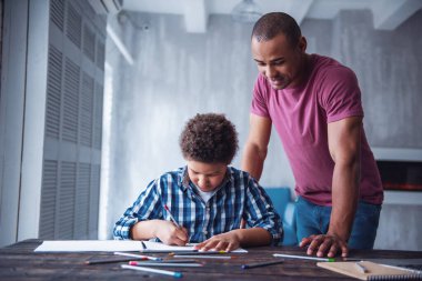 Yakışıklı adam evinde oğlunun çizimini izlerken gülümsüyor.