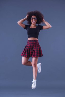 Şık bir kadın zıplıyor ve gülümsüyor, gri bir arka planda, tam boy