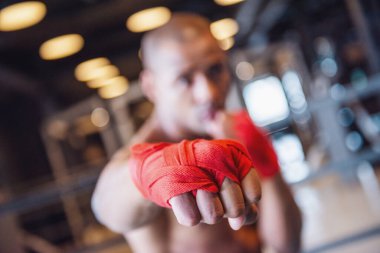 Yakışıklı genç boksör, elleri kırmızı bandajla sarılı, spor salonunda çalışıyor.