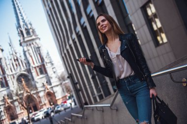 Tam uzunlukta rahat kıyafetler ve cep telefonda konuşurken ve şehir merkezinde yürürken gülümseyen güneş gözlüğü güzel genç kız portresi