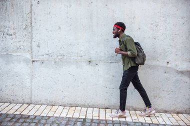Genç bir adam büyük bir duvarın yanında sırt çantasıyla köprüde yürürken kaldırımda yürüyor.