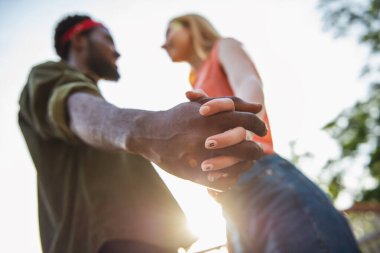 Genç, neşeli bir çift. Bir adam ve sarışın bir kadın gülümsüyor. Bir sokakta yürürken birbirlerinin ellerini tutuyorlar.