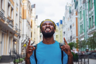 Genç bir adam köprünün sokaklarında sırt çantasıyla yürürken parmaklarını kaldırmaktan memnun.