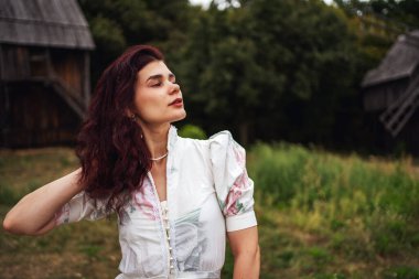 Retro tarzı. Ormanın arka planında beyaz bir elbise, değirmen ve kırmızı gün batımı giymiş siyah şık saçlı güzel bir kızın portresi..