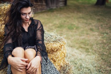 Retro tarzı. Siyah saçlı güzel bir kız, eski ahşap bir evin arka planında samanlığın yanında poz veriyor..