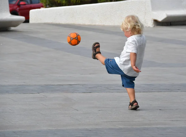 小男孩在空荡荡的街上踢足球 夏天带着球活动的孩子 — 图库照片
