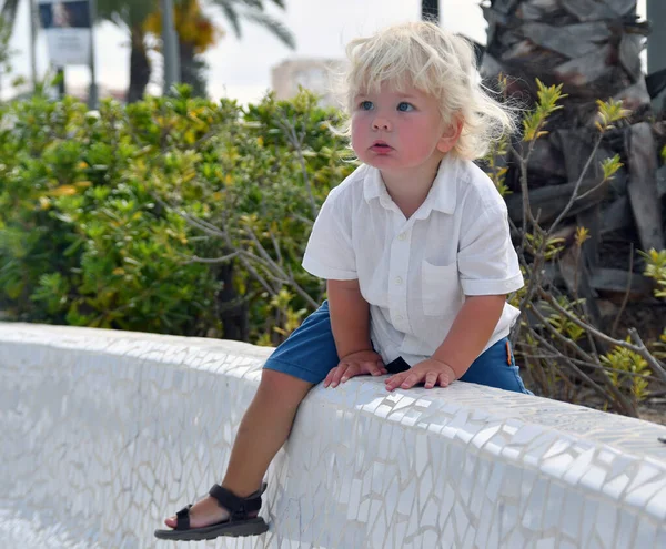 Cute ittle tomboy climbs out of the bushes. 2 years old blond caucasian boy.