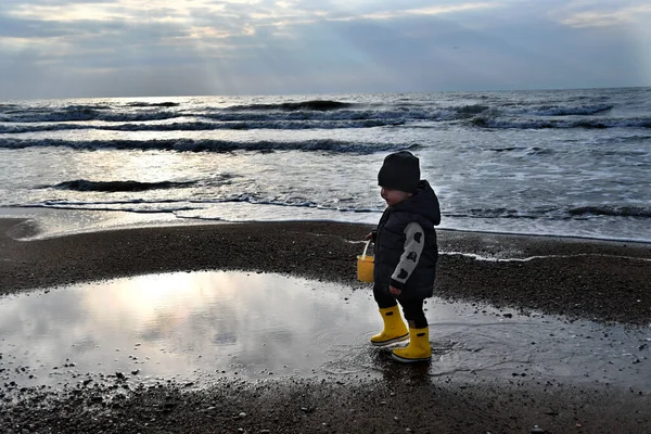 暖かいベストと黄色のゴムブーツを身に着けている小さな男の子は秋の季節に厳しいバルト海を歩く — ストック写真