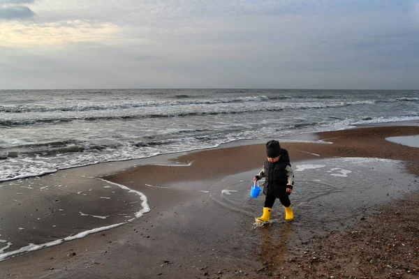 暖かいベストと黄色のゴムブーツを身に着けている小さな2年の男の子は秋のシーズンに厳しいバルト海を歩く — ストック写真