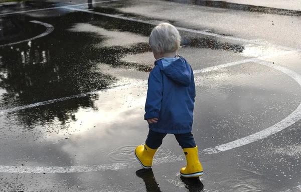 Mały Chłopiec Żółtych Gumowych Butach Przedzierający Się Przez Kałuże Deszczowy — Zdjęcie stockowe