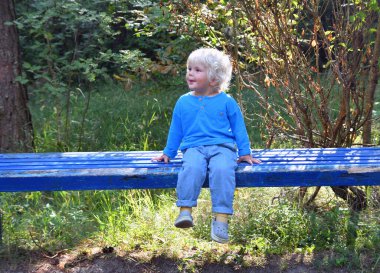 Parktaki mavi bankta oturan mavi tişörtlü şirin çocuk.