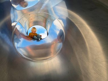 Yaratıcı oyun parkında metal borunun içine tırmanan küçük çocuk.