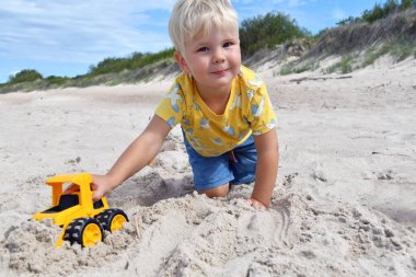 3-4 yaşlarında tatlı bir çocuk kumlu sahilde buldozerle oynuyor. 