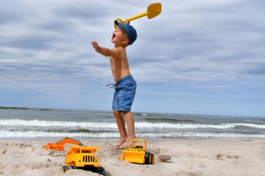 Kumlu Baltık sahilinde kürekle oynayan 3-4 yaşlarında etkileyici bir çocuk.