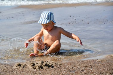 Küçük çocuk sahilde oturur ve suda oynar. Çocuklar için yaz etkinlikleri