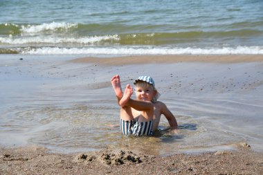 Küçük çocuk sahilde oturur ve suda oynar. Çocuklar için yaz etkinlikleri