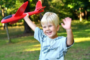 Oyuncak uçakla oynayan ve parkta elini sallayan 4 yaşındaki şirin çocuk. Çocuklar için yaz açık hava aktiviteleri