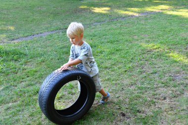 Küçük çocuk parkta lastikle oynuyor. Çocuklar için yaz açık hava aktiviteleri