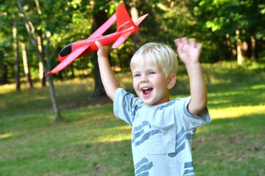 Oyuncak uçakla oynayan ve parkta elini sallayan 4 yaşındaki şirin çocuk. Çocuklar için yaz açık hava aktiviteleri