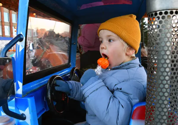 Mutlu çocuk, sonbahar sezonunda bir lunaparkta eski bir araba atlıkarıncaya binip lolipop yalıyor.