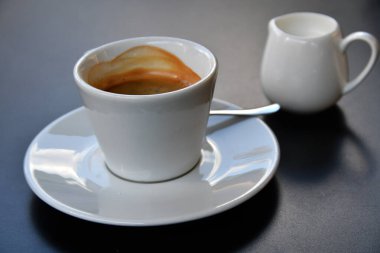 Minimalist beyaz bardakta sıcak espresso ve küçük sürahi süt.