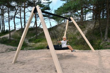 Litthe yakışıklı oğlan yaz mevsiminde bir parkta lastik sallanıyor.