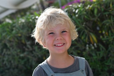 Gülümseyen sarışın çocuk. Yazın yeşillikte dışarıda 5 yaşında bir portre.