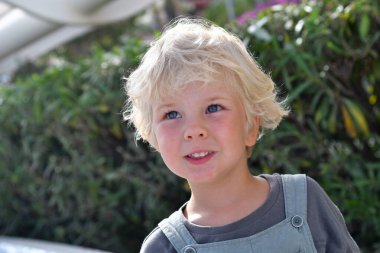 Gülümseyen sarışın çocuk. Yazın yeşillikte dışarıda 5 yaşında bir portre.