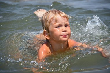 4-5 yaşlarında küçük bir çocuk yaz tatilinde deniz dalgalarında yüzer ve oynar.