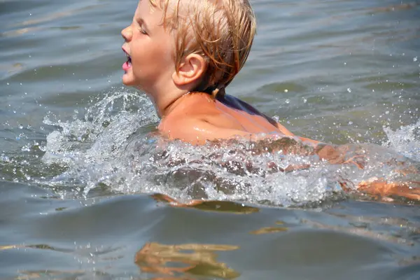 4-5 yaşlarında küçük bir çocuk yaz tatilinde deniz dalgalarında yüzer ve oynar.