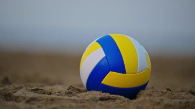Arkasında sakin okyanus dalgaları olan, kumlu sahilde dinlenen voleybol topunun 4K yavaş çekim sahnesi huzurlu bir sahil anın özünü yakalıyor..