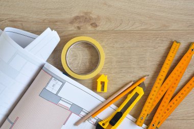 Architectural drawings and pencils, ruler, clerical knife, scotch tape on wooden background. Top view. Repair housing concept. 