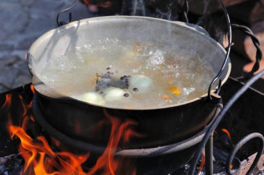 Avludaki kazıkta çorbayla birlikte dökme demir kazan. Açık ateşte yemek pişirmek. Et, sebze ve baharatlı çorba.