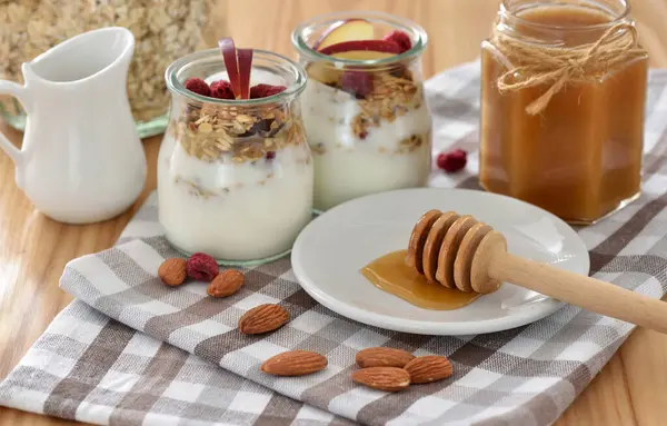 木のテーブルのガラス瓶にヨーグルト リンゴ ナッツ 蜂蜜が付いているクランチ グラノーラ 健康的な朝食のコンセプト ストック写真
