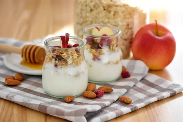 木のテーブルのガラス瓶にヨーグルト リンゴ ナッツ 蜂蜜が付いているクランチ グラノーラ 健康的な朝食のコンセプト ストックフォト