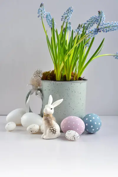 复活节作曲用白兔 鸡蛋和淡蓝色麝香在杯子中绽放 复活节静物 免版税图库照片