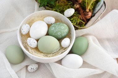 Süslü paskalya yumurtaları beyaz bir kâse içinde açık ahşap bir masanın üzerinde keten kumaş üzerinde. Mutlu Paskalyalar