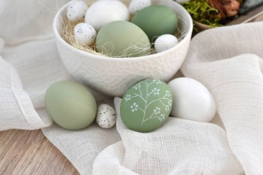 Süslü paskalya yumurtaları beyaz bir kâse içinde açık ahşap bir masanın üzerinde keten kumaş üzerinde. Mutlu Paskalyalar