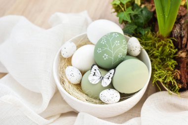 Süslü paskalya yumurtaları beyaz bir kâse içinde açık ahşap bir masanın üzerinde keten kumaş üzerinde. Mutlu Paskalyalar