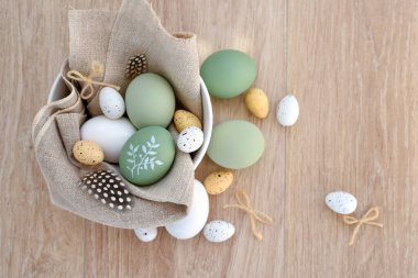 Süslü paskalya yumurtaları beyaz bir kâse içinde açık ahşap bir masanın üzerinde keten kumaş üzerinde. Üst Manzara. Metnin için boşluk ile