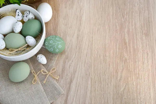Süslü paskalya yumurtaları beyaz bir kâse içinde açık ahşap bir masanın üzerinde keten kumaş üzerinde. Üst Manzara. Metnin için boşluk ile