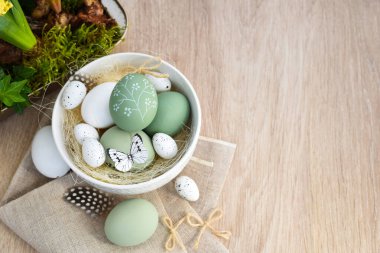 Süslü paskalya yumurtaları beyaz bir kâse içinde açık ahşap bir masanın üzerinde keten kumaş üzerinde. Üst Manzara. Metnin için boşluk ile