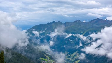 Dağların üzerinde fırtına bulutları. Yeşil çayırlar, dağınık yerleşim yerleri ve etkileyici ve ilginç bulutların altında karanlık ormanlar..